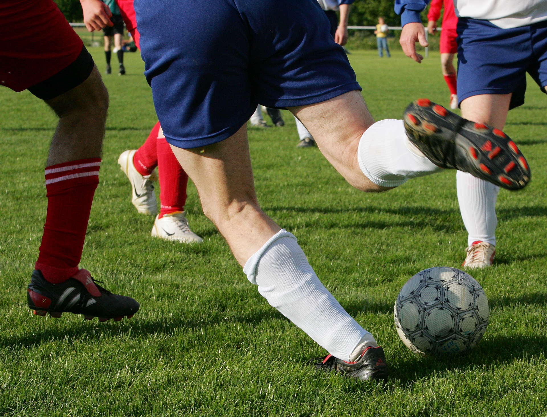 Fußballspieler auf dem Sportplatz, einer davon schießt den Ball. 